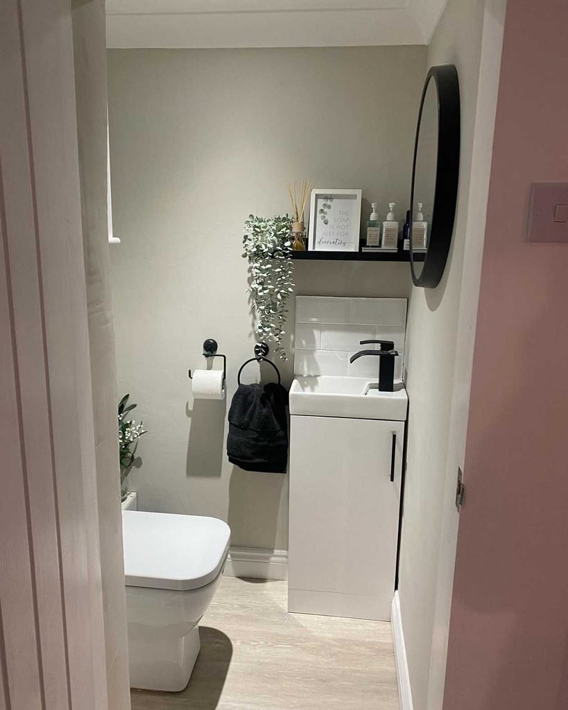 Adding black accents is an easy way to give a small toilet room a stylish and contemporary upgrade. This design uses black fixtures, a round mirror frame, and matching accessories to create a strong contrast against the soft neutral walls.
