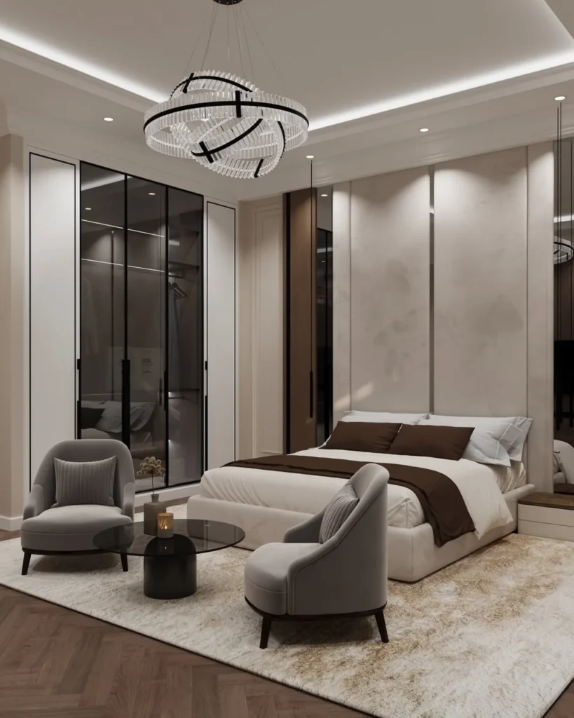 Cream bed with brown throw, two grey armchairs and a crystal ring chandelier in a bedroom