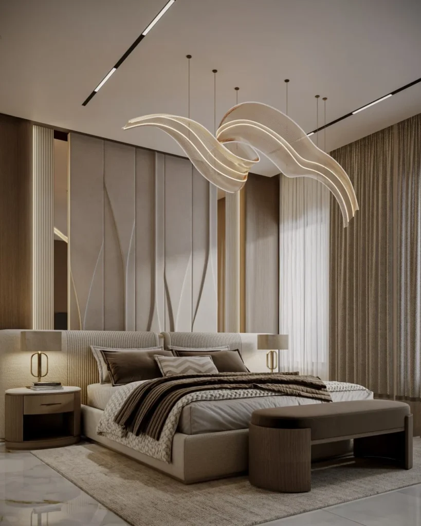 Ribbon-shaped glowing pendant above a taupe bed with a sculpted padded wall and brown bench