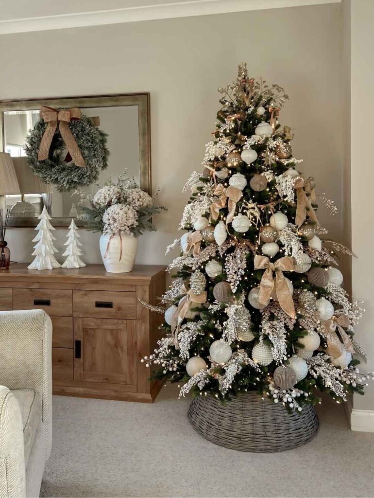 Elegant Christmas tree decorated with champagne gold ribbon bows, ivory baubles, frosted berry sprays, warm lights, and a woven tree collar.