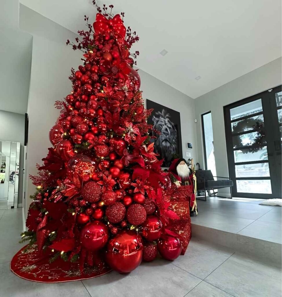 Tall all-red Christmas tree with oversized glossy baubles, glitter ornaments, red poinsettias, berry sprays, and a sparkling red bow topper.