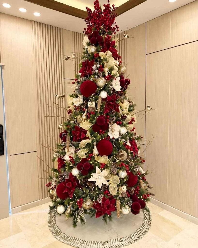Burgundy and gold Christmas tree decorated with red poinsettias, velvet-look baubles, champagne ribbons, white flowers, berry branches, and bird ornaments