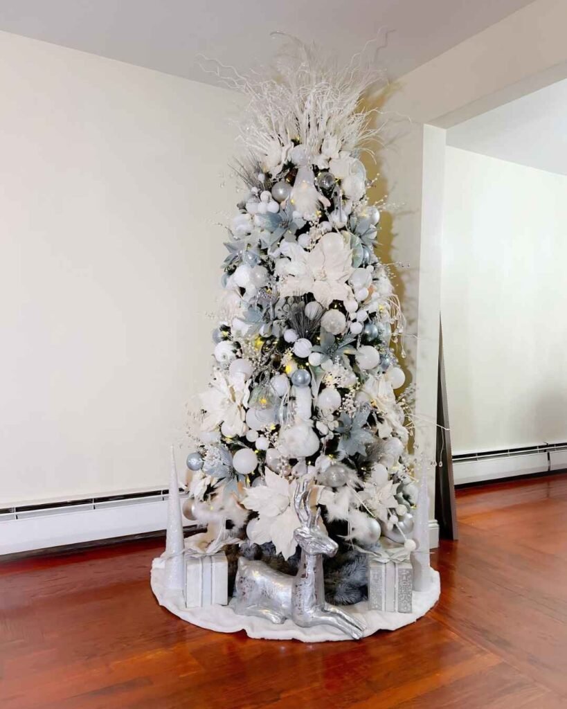 Frosted white and silver Christmas tree with white poinsettias, icy blue ornaments, snowy branches, silver reindeer, and decorative gifts.