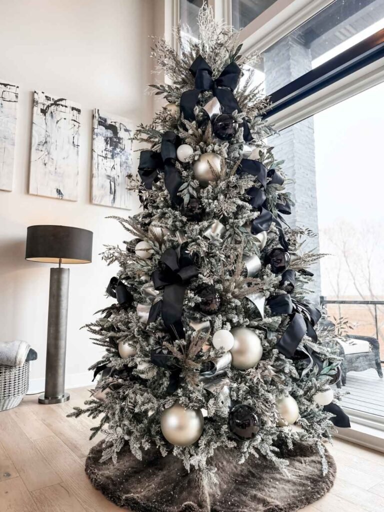 Flocked Christmas tree decorated with black satin bows, glossy black ornaments, champagne silver baubles, metallic foliage, and a dark plush tree skirt.