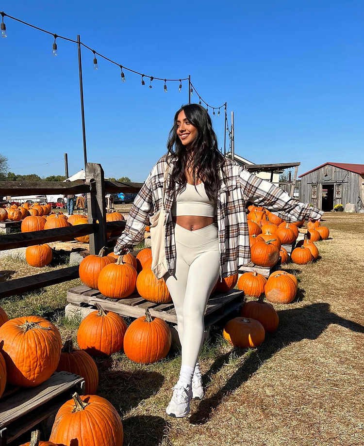 Woman walking through a pumpkin patch in a cream matching crop top and leggings set, oversized brown plaid shirt, white crew socks, and white sneakers.
